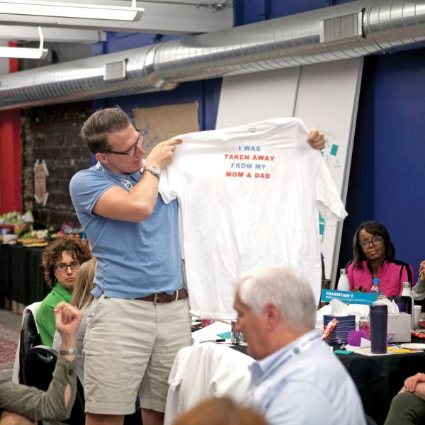 Man holding a t-shirt at the Ten for Ten conference that reads "I was taken away from my mom and dad"