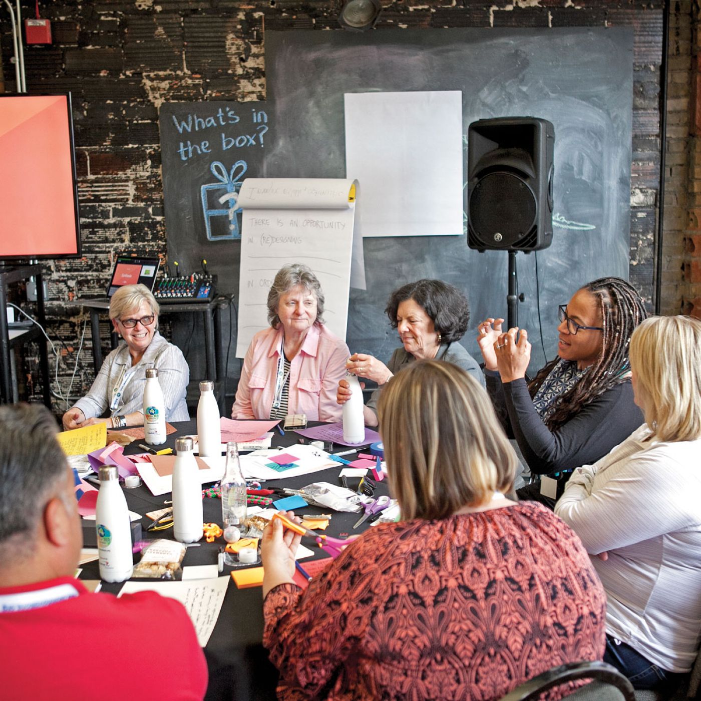 Group of people sitting around a table and actively discussing something, "We can’t simply tweak things and expect it to get better." Shenandoah Chefalo